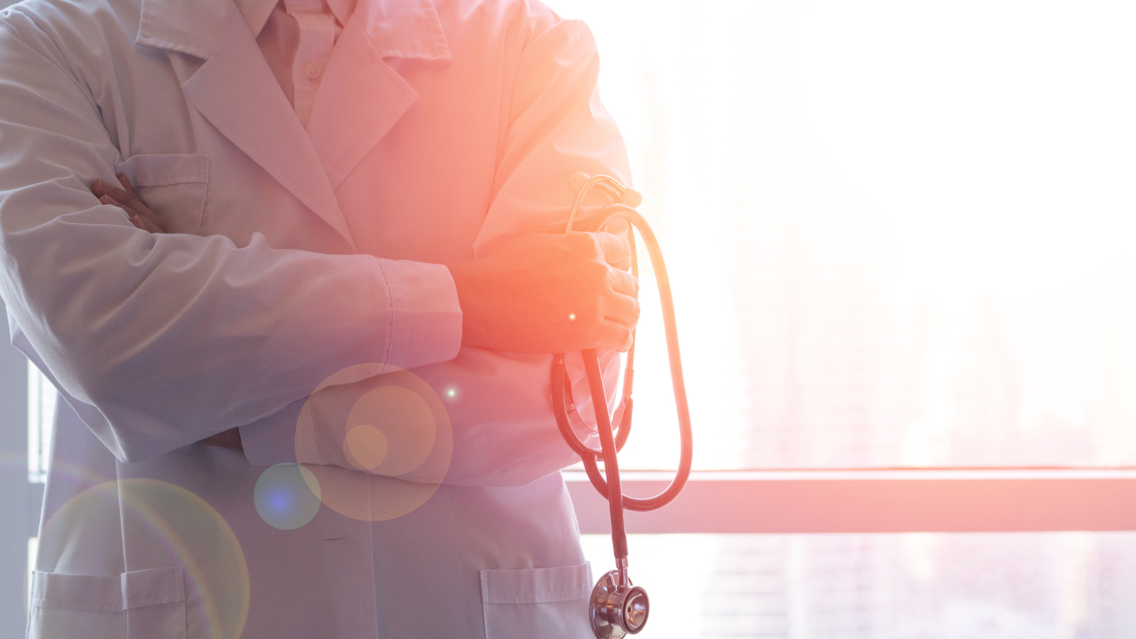 Close up of doctor’s crossed arms holding a stethoscope and wearing a white lab coat
